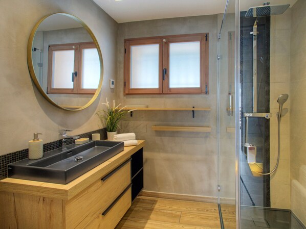 Ein modernes Badezimmer mit einem großen Waschbecken, einem Spiegel, einer Dusche und Holzausbau.