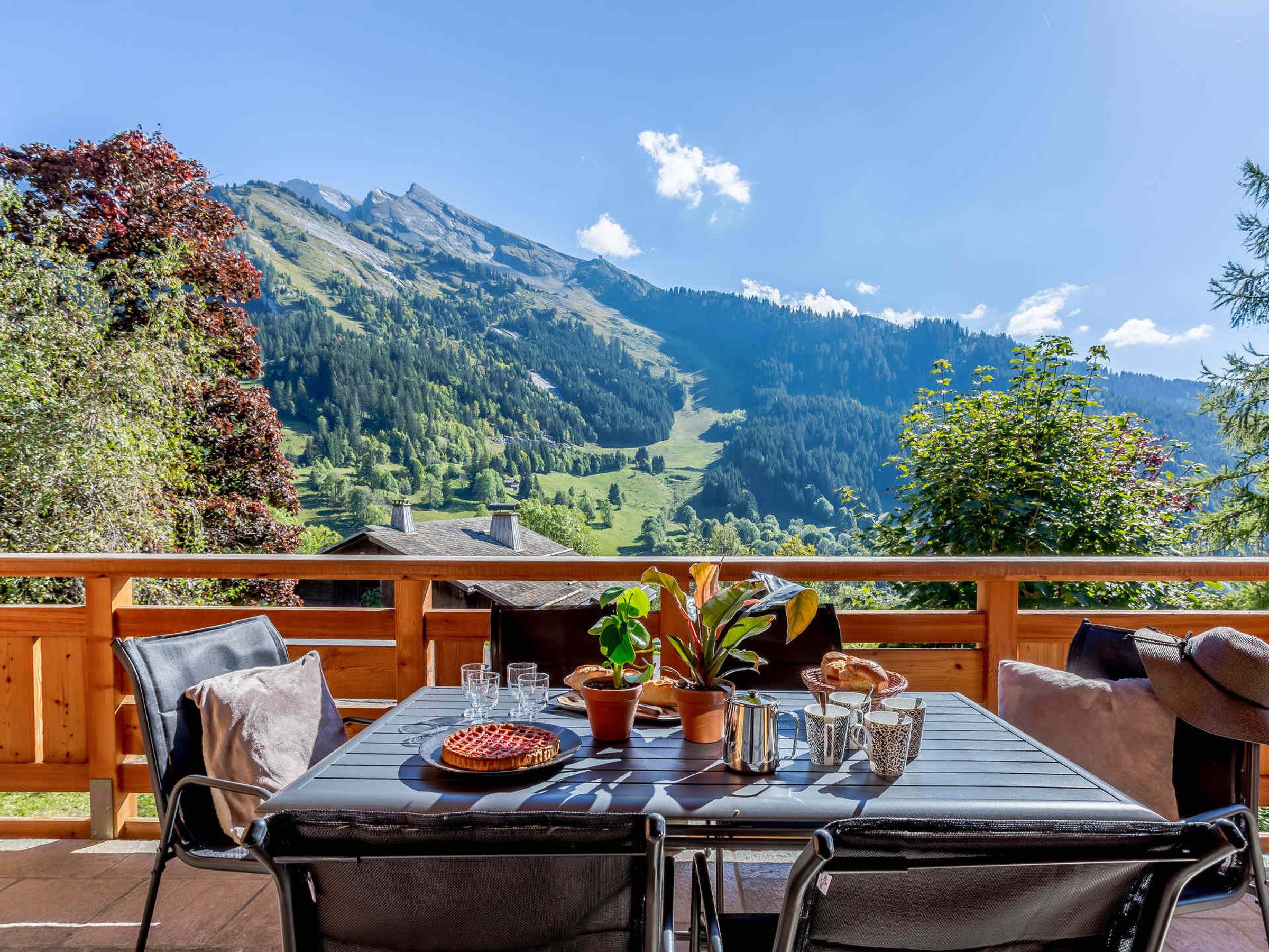 Eine Holzdielen-Terrasse mit Tisch für zwei Personen, mit Blick auf eine gebirgige Landschaft.