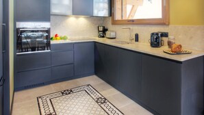 A modern kitchen with dark cabinets, a built-in oven, a coffee maker, and a window above the sink.