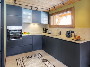 A modern kitchen with dark cabinets, a built-in oven, a coffee maker, and a window above the sink. - Luxury chalet 5★, 6 pers, hammam, near slopes, 3 bedrooms (La Clusaz)