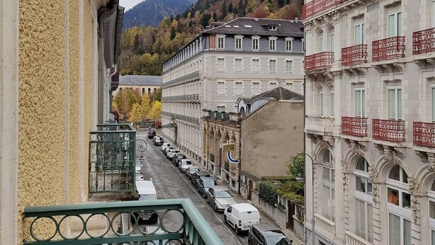 A street view with buildings, a mountain in the background, and parked cars. - Studio 2/4 pers near center and cable car (Cauterets)