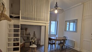 A room with a loft bed, a dining area with a table and chairs, a hanging light fixture, and a window with a view. - Studio 2/4 pers near center and cable car (Cauterets)
