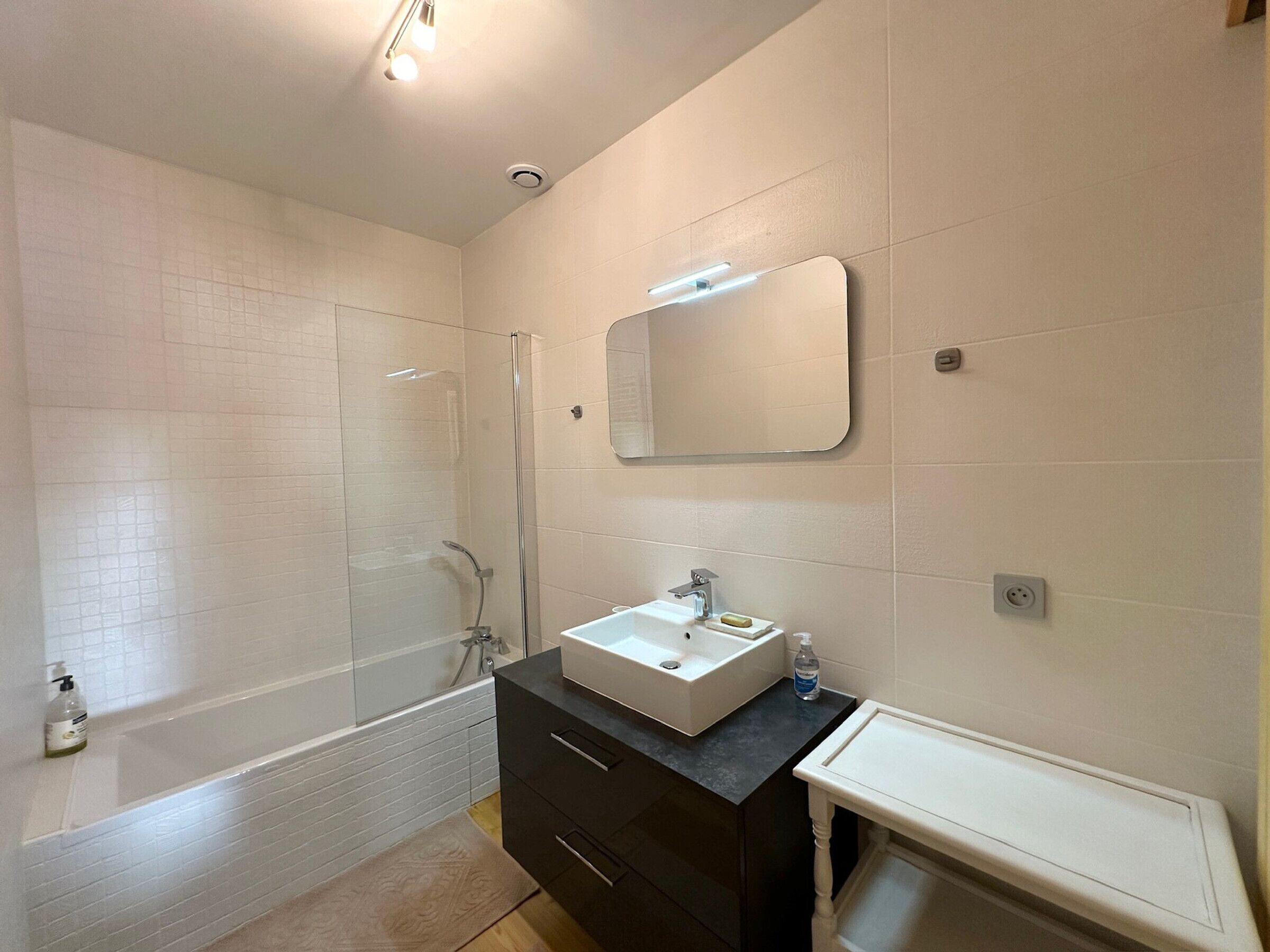 A modern bathroom with a glass-enclosed shower, a white sink with a mirror above it, and a dark vanity with drawers.