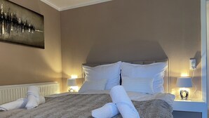 A neatly made bed with white linens and a fluffy gray blanket, two bedside lamps, and a painting on the wall.