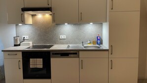 A modern kitchen with a built-in oven, a dishwasher, and a sink. There is a kettle and a bottle of dish soap on the counter.