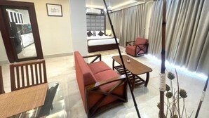A modern hotel room with a glass dining table, red upholstered chairs, a sofa, and a bed with a headboard. - The Crystal Newtown Kolkata (Barasat)