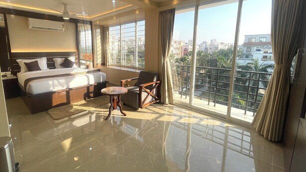 A modern hotel room with a large bed, a desk, a chair, and a balcony with a city view. - The Crystal Newtown Kolkata (Barasat)