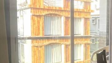 Una habitación con un gran ventanal corredizo que da a un balcón. El balcón tiene barandilla metálica y vistas a un edificio con balcones de madera.