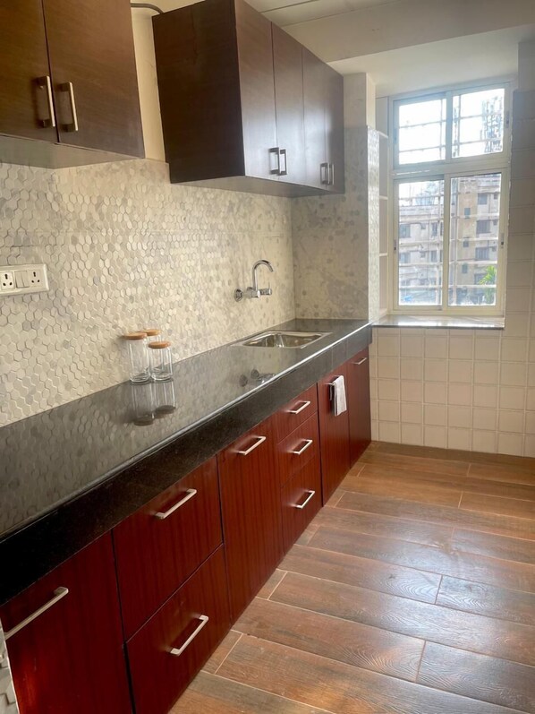 A kitchen with wooden cabinets, a black countertop, and a window with a view of buildings.
