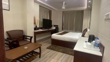 Una habitación de hotel con cama, escritorio, silla, televisor y ventilador de techo.