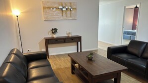 A living room with a dark wooden coffee table, two black leather sofas, a wooden side table with decorative items, and a large abstract painting on the wall.