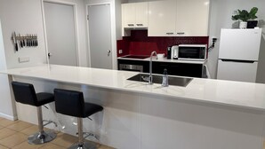 A modern kitchen with white cabinets, a red backsplash, a stainless steel sink, and a white refrigerator.