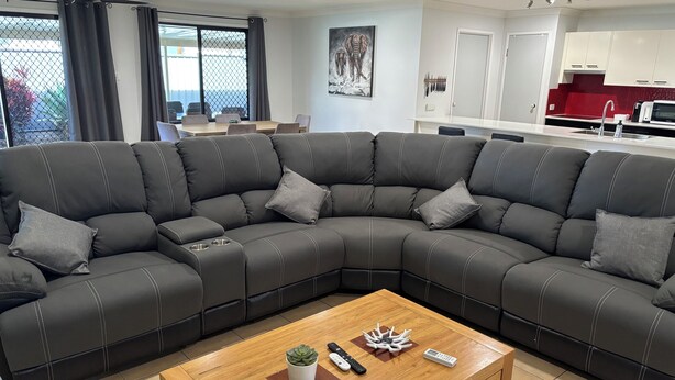 A modern living room with a large L-shaped sectional sofa, a wooden coffee table, and a kitchen area in the background.