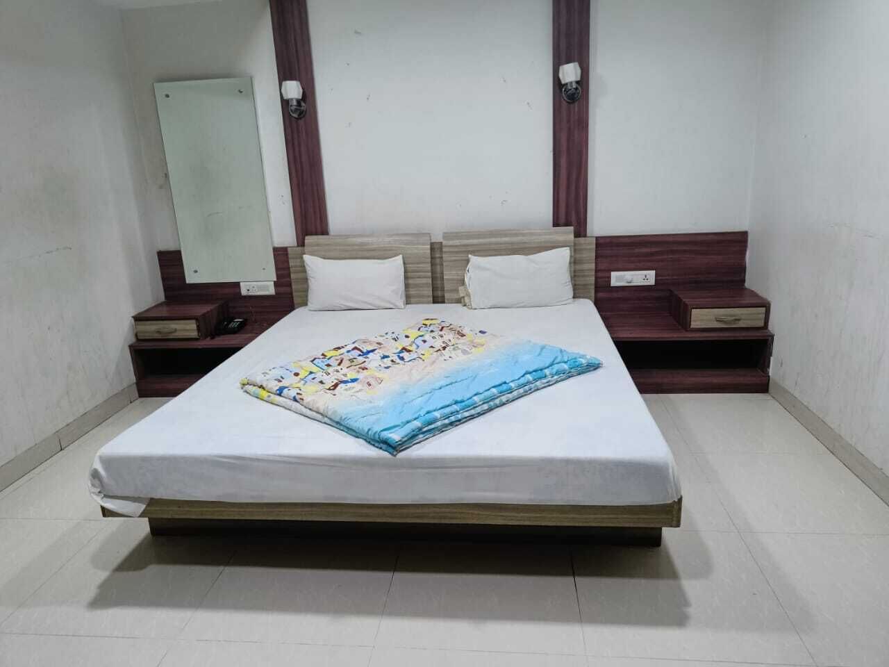 A single bed with a blue and white quilt, wooden headboard, two bedside tables with lamps, and a mirror on the wall.