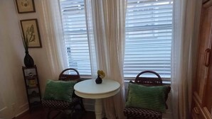 Un dormitorio con una cama, dos sillas, una mesita y un ventanal con cortinas.