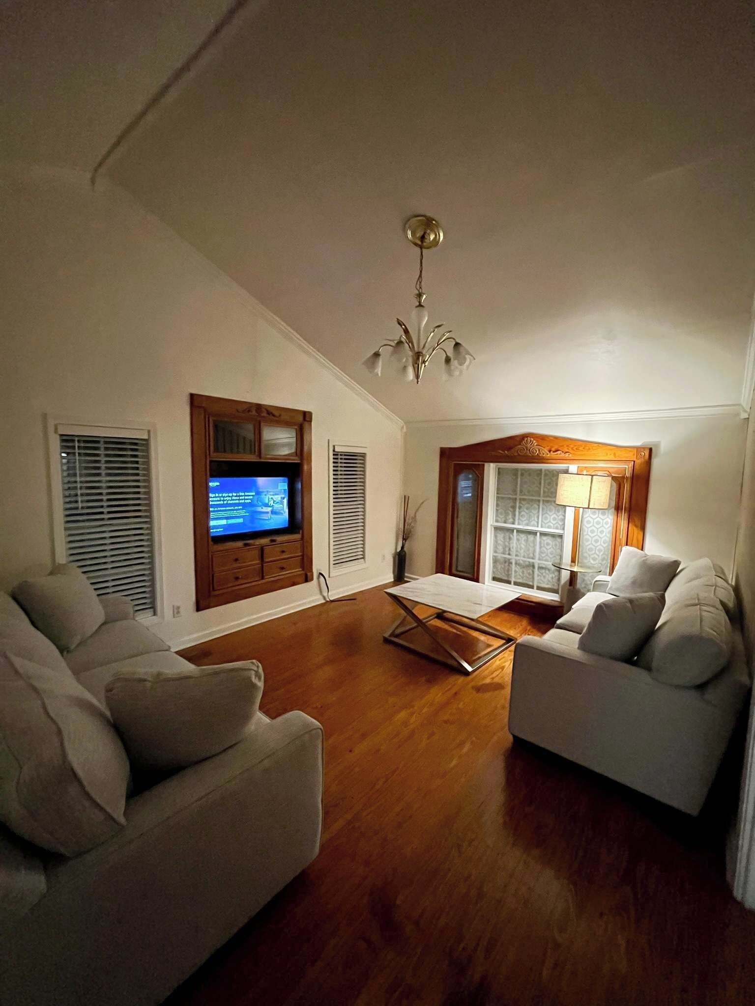 Una sala de estar con piso de madera, un televisor sobre un mueble de madera, un candelabro y dos sofás.