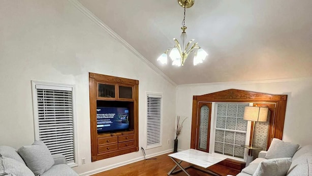 Ein geräumiges Wohnzimmer mit Holzboden, zwei grauen Sofas, einem Couchtisch und einem an einer Holzkommode befestigten Fernseher.