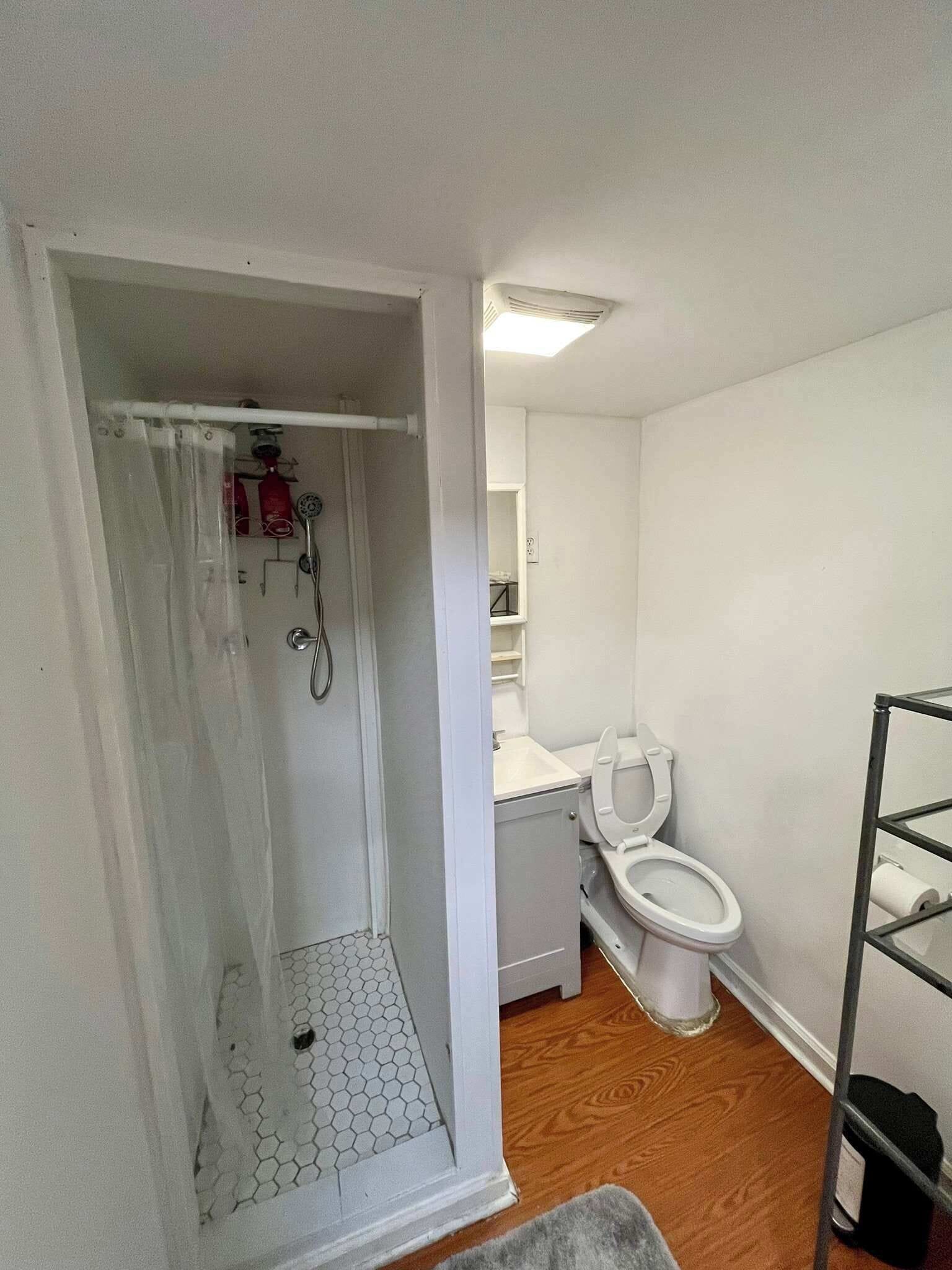 Un baño con ducha, inodoro y una estantería metálica.