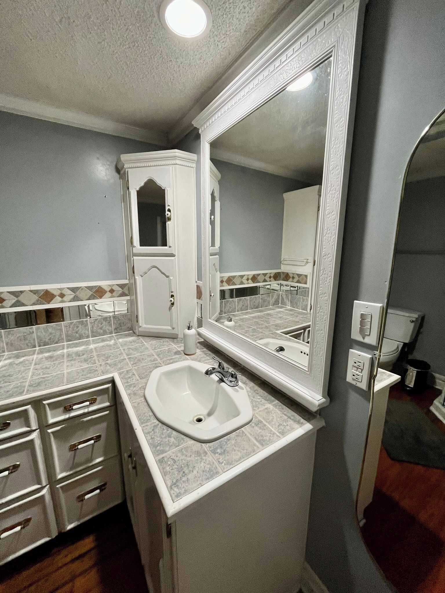 A bathroom with a sink, mirror, cabinet, and tiled floor.