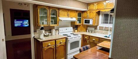 A compact kitchen with wooden cabinets, a stove, a microwave, and a dining area with a table and chairs.