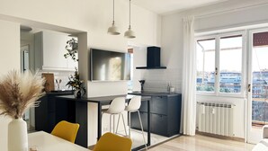 Une cuisine moderne équipée d’un téléviseur, d’un coin repas avec des chaises et offrant une vue sur la ville grâce à de grandes fenêtres.
