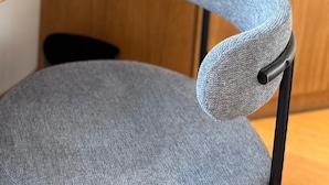 A chair with a grey fabric backrest and a wooden shelf in the background. - Ma.maison (Guémar)