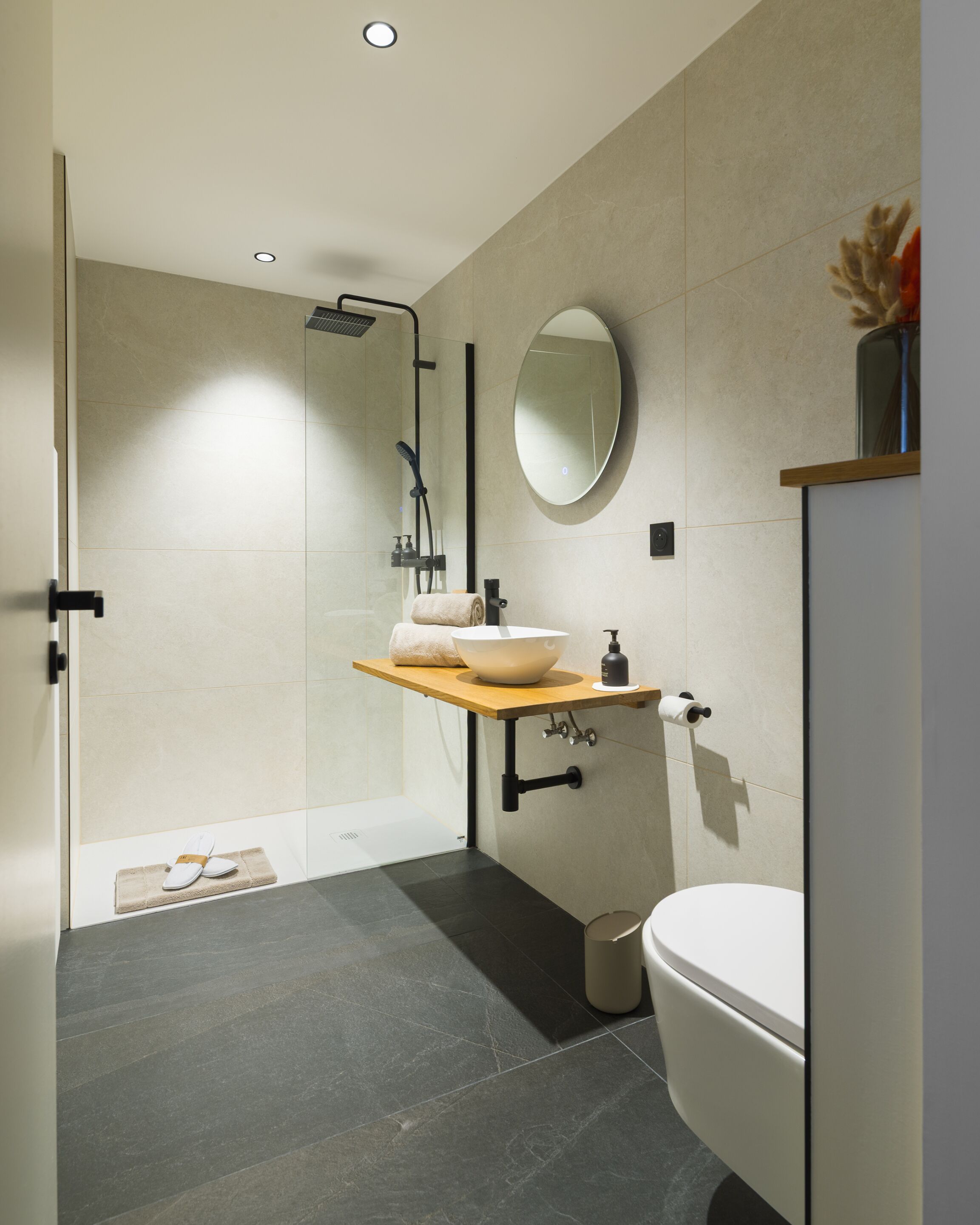 Ein modernes Badezimmer mit einer Duschkabine aus Glas, einem Holzbadezimmer-Möbelstück, einem runden Spiegel und einer weißen Toilette.
