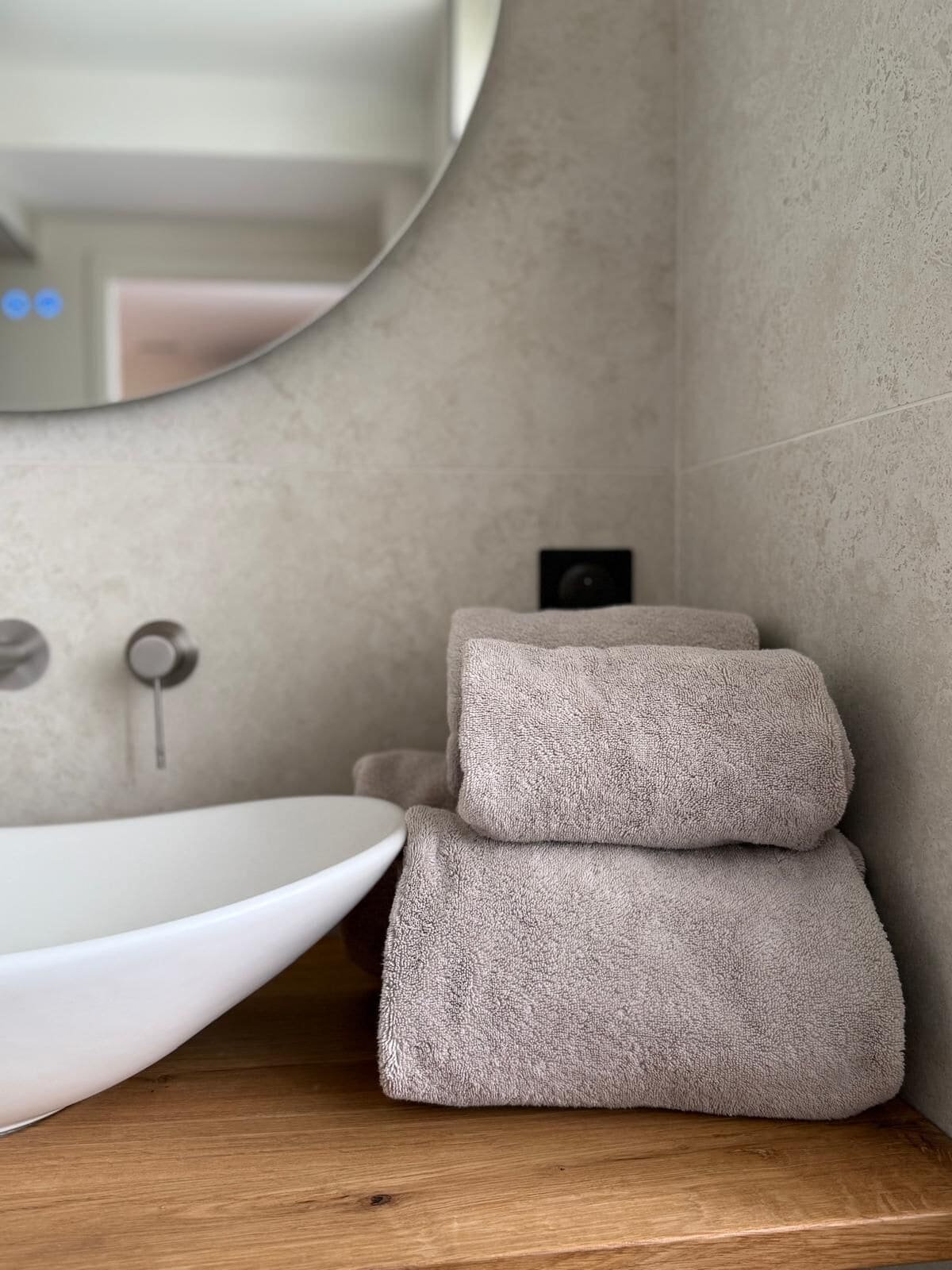 A bathroom with a round mirror, a white sink, and two stacked towels on a wooden countertop.