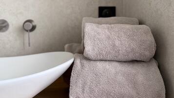 A bathroom with a round mirror, a white sink, and two stacked towels on a wooden countertop.