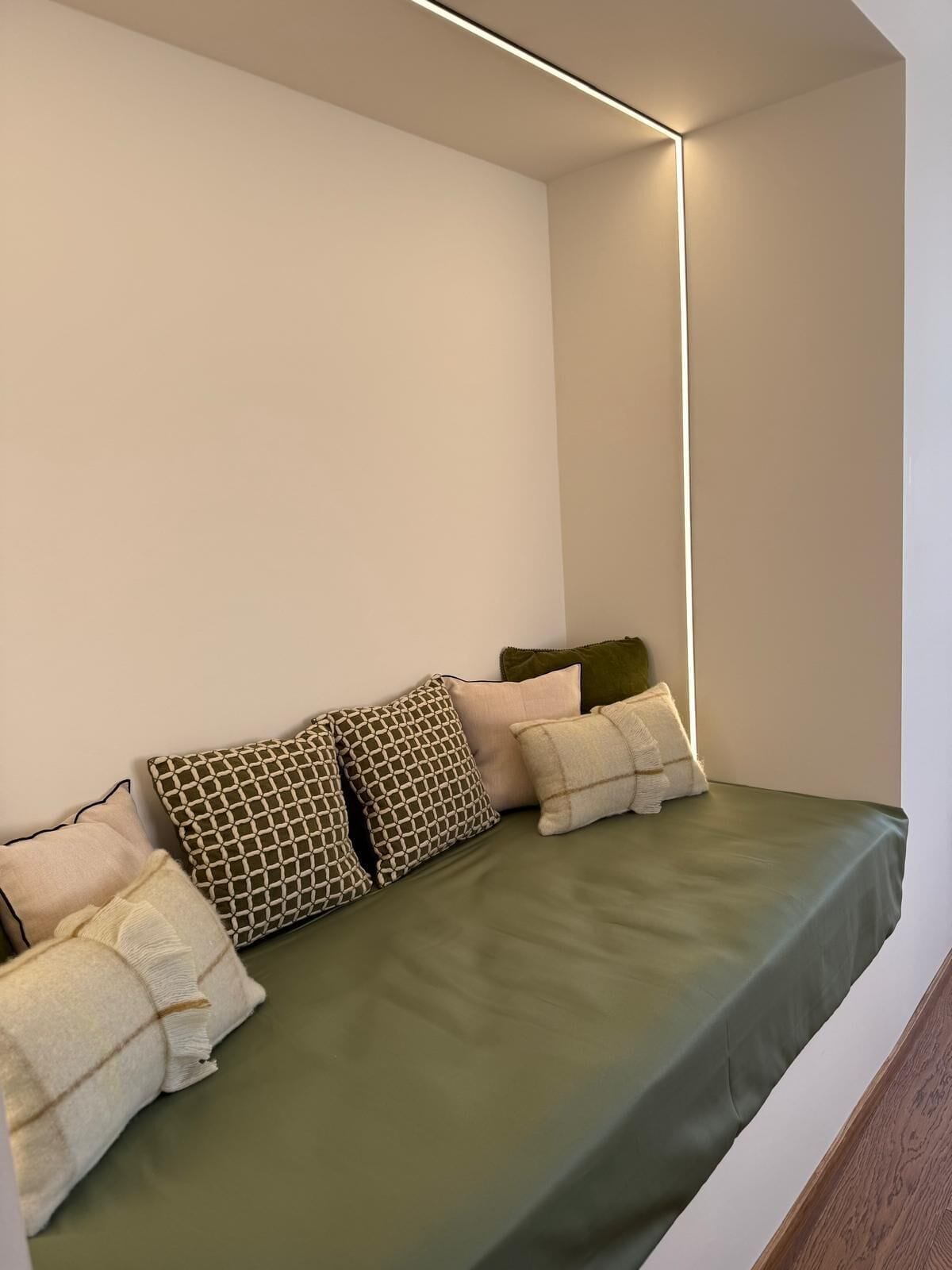 A small, cozy room with a green bed, white walls, and a modern light fixture.