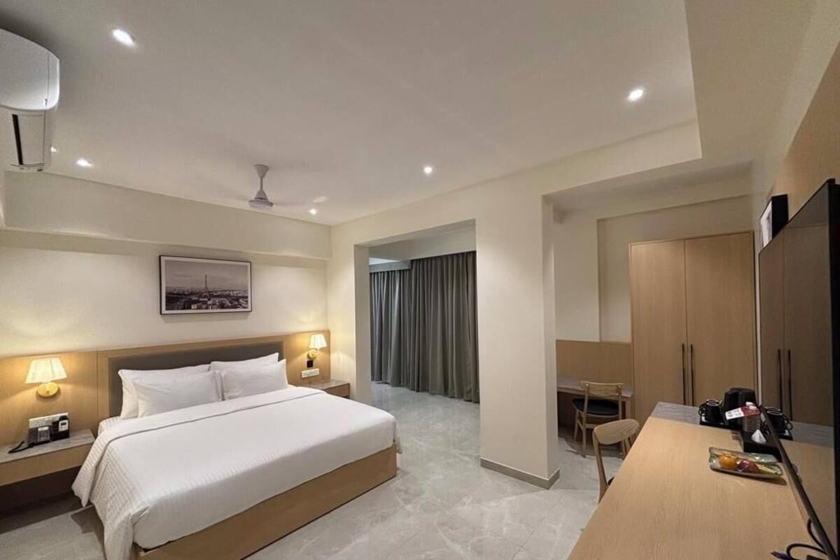 A hotel room with a large bed, bedside lamps, a desk with a chair, a mirror, and a view of the city through the window.
