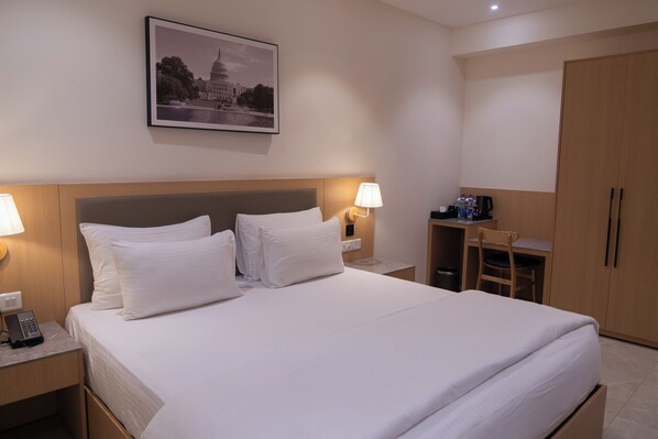 Habitación de hotel con cama, dos lámparas de noche, un escritorio con silla, armario y un cuadro en la pared.