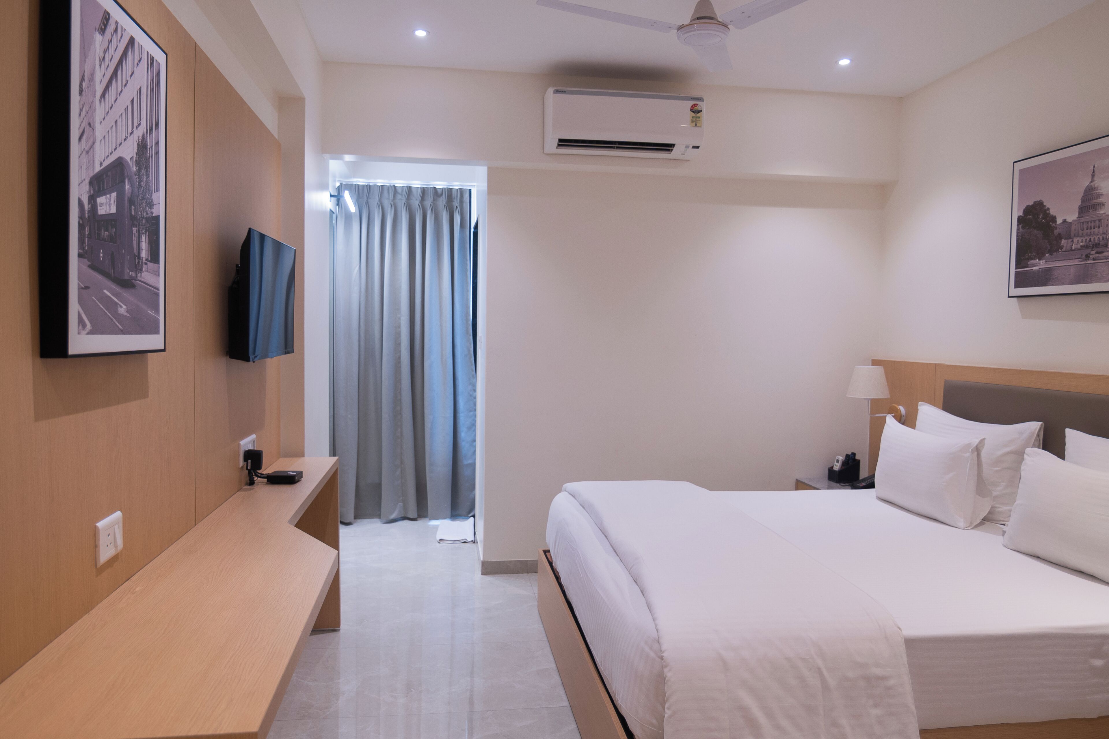 Ein Hotelzimmer mit Bett, Schreibtisch, Flachbildfernseher, Klimaanlage und einem fenster mit Vorhängen.