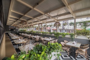 Un espacio cubierto al aire libre con mesas y sillas, ventiladores de techo y plantas colgantes.