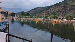 Vista a la orilla del río con barcos, una estructura de madera y montañas al fondo.