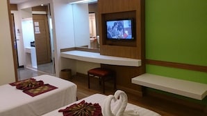 Habitación de hotel con dos camas, un televisor fijado en la pared, un taburete pequeño y una pared de acento verde.
