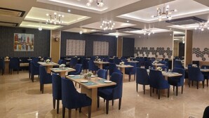 Uma sala de jantar espaçosa, com várias mesas e cadeiras, iluminação no teto e detalhes decorativos nas paredes.