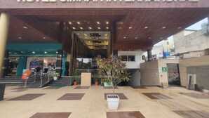 Entrada do Hotel Simran International com design moderno, apresentando uma grande placa, escadaria e plantas em vasos.