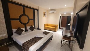 Quarto de hotel com uma cama grande, uma mesa com televisão de tela plana, um sofá e um aparelho de ar condicionado.