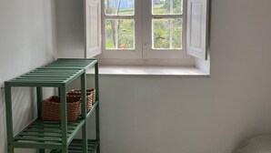 Une pièce avec une fenêtre blanche, une étagère en métal verte avec des paniers, et un sol imitant la pierre.