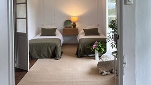 Une chambre avec deux lits, une table de chevet avec une lampe, un luminaire au plafond et une fenêtre donnant sur un paysage verdoyant.