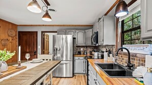 A modern kitchen with stainless steel appliances, wooden countertops, and a large window providing natural light. - 3BR Gatlinburg*Firepit*Hot Tub*Privacy + Quiet! (Gatlinburg)