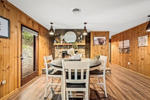 Una habitación con paneles de madera, una chimenea de piedra, una mesa redonda con sillas y un espejo grande sobre la chimenea.