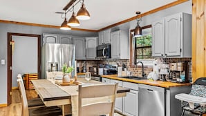 A modern kitchen with grey cabinets, stainless steel appliances, and a wooden dining table. - 3BR Gatlinburg*Firepit*Hot Tub*Privacy + Quiet! (Gatlinburg)