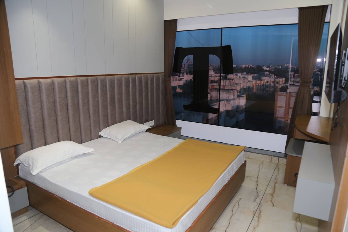 Quarto de hotel com uma cama grande, vista para a cidade pela janela e cabeceira de madeira.