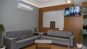 Un área de espera moderna con un conjunto de sofá gris, una mesita de centro pequeña y un televisor montado que muestra varias tomas de cámara.
