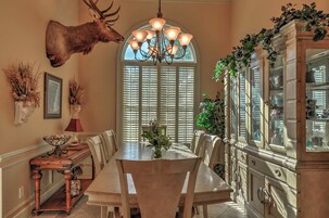 Un comedor con una mesa grande, sillas, una araña y una cabeza de ciervo montada.