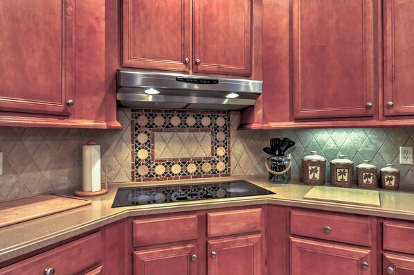A kitchen with wooden cabinets, a stainless steel range hood, a patterned backsplash, and a countertop with kitchen utensils and jars. - Walk to Marina! Midway House by Sunbury Channel (Midway)