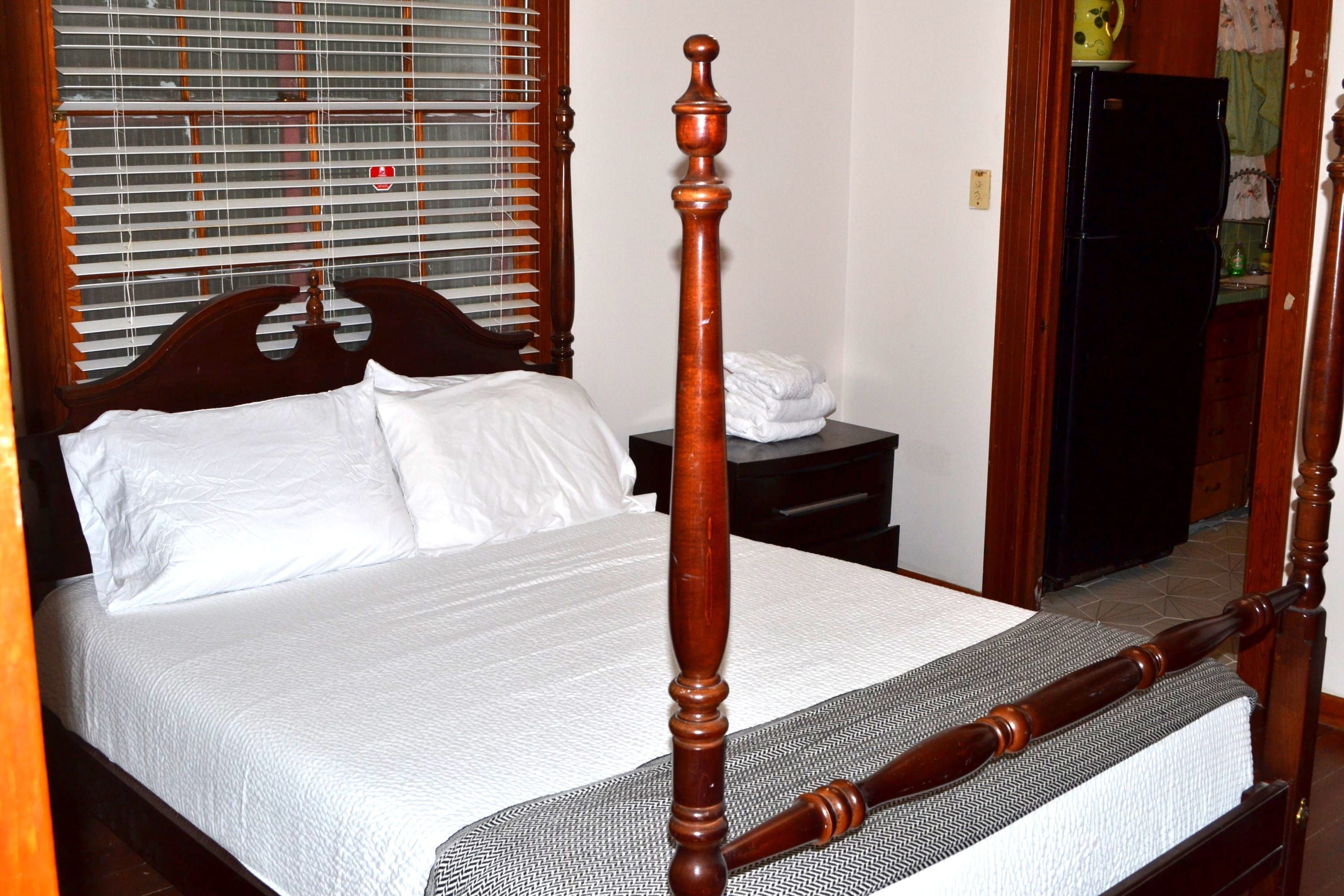 Una cama con dosel y tablero de madera, una colcha blanca y piecero a juego.