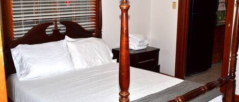 Una cama con dosel y tablero de madera, una colcha blanca y piecero a juego.